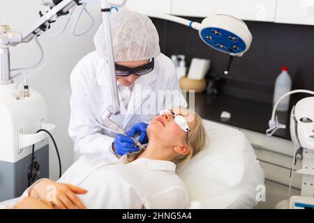 Cosmetologiste expérimenté effectuant un traitement laser du visage à la jeune femme Banque D'Images