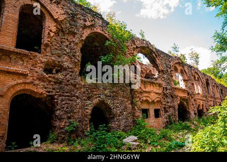 Ruines d'une ancienne forteresse abandonnée entourée de plantes vertes le jour ensoleillé Banque D'Images