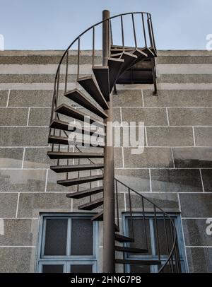 L'escalier en colimaçon en métal brun avec rambarde en fer mène du balcon sur le toit au premier étage devant un mur texturé en briques. Mise au point sélective. Banque D'Images