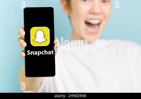 Février 2022 - Tallinn, Estonie. Un garçon souriant et inconcentré avec un smartphone affichant le logo de l'application Snapchat Banque D'Images