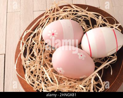 Trois œufs de Pâques roses dans un nid sur une table en bois, concept traditionnel de Pâques Banque D'Images