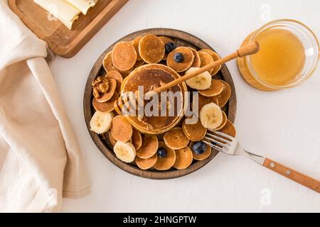 Petit déjeuner tendance original sur un grand plateau rond en bois, assortiment de crêpes avec miel, banane et noix. Vue du dessus Banque D'Images