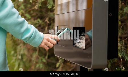 Une femme utilise un terminal libre-service de rue pour le paiement sans contact avec un smartphone. Banque D'Images