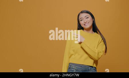 Adulte positif pointant sur le côté gauche du studio devant l'appareil photo avec l'index, indiquant les directions et faisant des suggestions. Femme souriant et regardant de côté, avec index. Banque D'Images