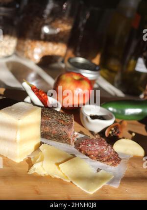 Salami au poivre sur plateau avec fromage anglais et irlandais, pommes en tranches et épices dans une cuisine rustique avec fenêtre de la cuisine Banque D'Images