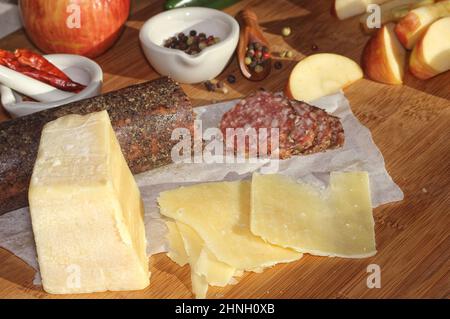 Salami au poivre sur plateau avec fromage anglais et irlandais, pommes en tranches et épices dans une cuisine rustique avec fenêtre de la cuisine Banque D'Images