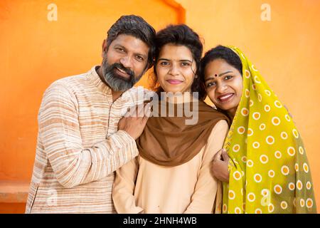 Portrait d'une famille indienne rurale heureuse, jeune fille en uniforme scolaire avec ses parents, Beard homme et femme à sari debout avec sa fille Banque D'Images