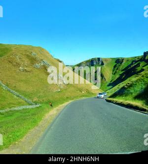 Voitures grimpant sur la colline escarpée (plus de 28 % ou 1 en 31⁄2) au col Winnats, Peak District, (près de Castleton, Derbyshire) au Royaume-Uni. La gorge de calcaire se trouve près de l'entrée de quatre grottes de touristes, l'une d'entre elles la caverne de Speedwell n'est accessible qu'en utilisant des bateaux. Les autres sont Peak Cavern, Treak Cliff Cavern et Blue John Cavern /mine. Le passage est soi-disant hanté par un jeune couple qui a été assassiné et volé là par des mineurs et leurs corps (découverts plus tard) ont été cachés dans les grottes. Banque D'Images