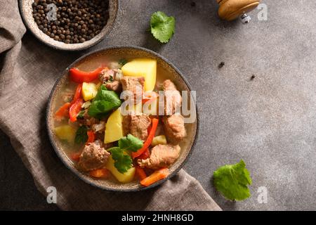 Ragoût de bœuf avec légumes, pommes de terre, poivre, carottes dans un bol sur fond marron. Cuisine européenne. Vue de dessus. Banque D'Images