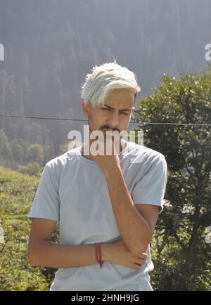 Vue de face d'un jeune homme aux cheveux blancs teints posant avec sa main sur le menton en regardant à l'extérieur avec l'espace de copie Banque D'Images