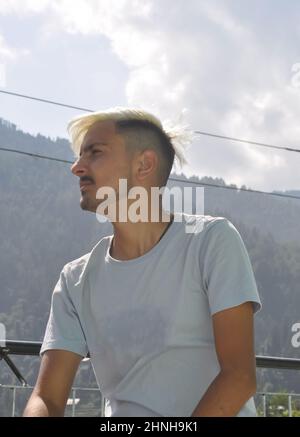 Vue en contre-plongée d'un jeune homme avec des cheveux blancs teints en regardant sur les côtés tout en étant assis à l'extérieur avec un espace de copie Banque D'Images