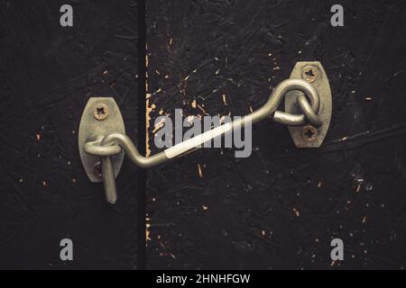 Ancienne porte en bois peint en noir, fermée sur un crochet en métal d'époque. Banque D'Images