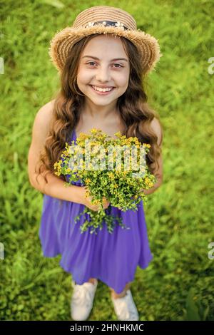 Joyeux bébé fille porter un chapeau de soleil sur les cheveux à long chemin et la mode robe d'été tenant des fleurs paysage naturel, boutique florale Banque D'Images