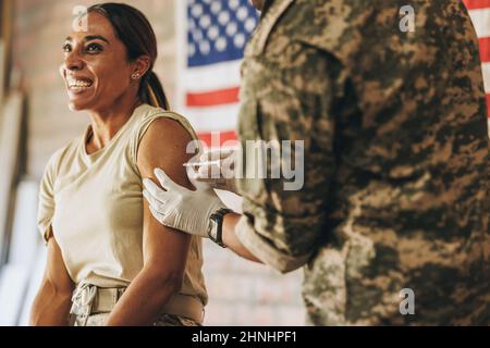 Une femme heureuse reçoit une dose du vaccin Covid-19 à l'hôpital militaire. Le militaire américain souriait volontiers en se faisant inj Banque D'Images