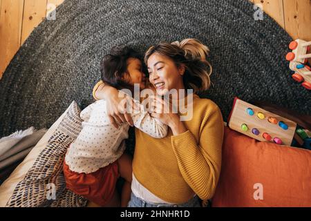 Vue en hauteur d'une mère et de sa fille couchée sur le sol dans leur aire de jeux. Une mère affectueuse souriant avec joie tout en embrassant sa fille. Mo Banque D'Images