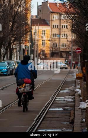 Vers 2022: Homme plus âgé sur un vélo à Sofia, Bulgarie. Ville, image urbaine. Un homme conduit un vélo sur les lignes de tramway dans une rue. Couleurs chaudes. Photo de haute qualité Banque D'Images
