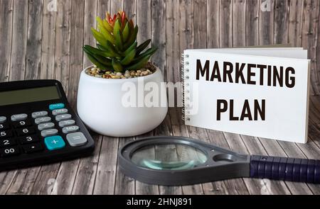 Plan de marketing écrit dans un bloc-notes, une table en bois avec une calculatrice, une loupe et un stylo. Image de concept pour l'en-tête ou l'image d'en-tête de blog. Banque D'Images