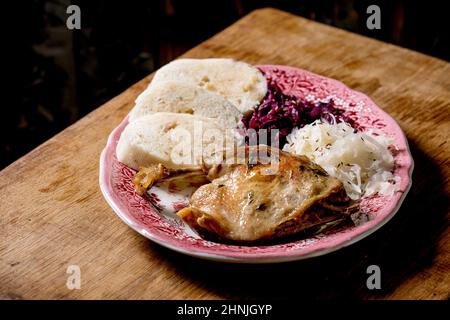 Pattes de canard cuites au four avec des pétrir de pain cuit en tranches et de la choucroute dans une assiette en céramique sur une table en bois brun. cuis traditionnel tchèque, allemand et européen Banque D'Images