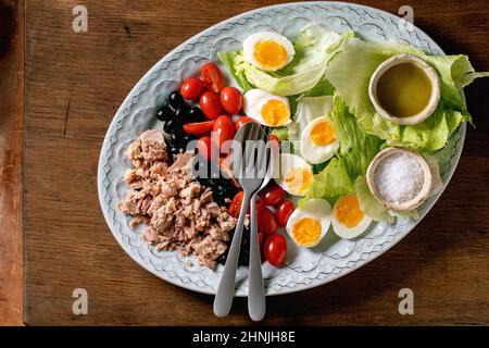 Salade française niçoise avec thon en conserve, olives et œufs, servie avec une vinaigrette à l'huile d'olive et du sel de mer sur une assiette en céramique sur un fond de bois Banque D'Images