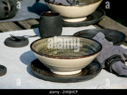 Table rustique à l'extérieur dans le jardin avec vaisselle en céramique artisanale vide, assiettes noires et bols rugueux, décorations de citrouille, sur la table en lin Banque D'Images