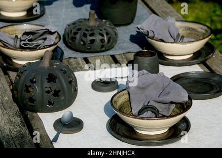 Table rustique à l'extérieur dans le jardin avec vaisselle en céramique artisanale vide, assiettes noires et bols rugueux, décorations de citrouille, sur la table en lin Banque D'Images