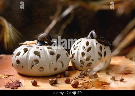 Décorations d'Halloween ou de Thanksgiving, ensemble de citrouilles blanches en céramique sculptées à la main, debout sur une table en pierre orange avec des feuilles d'automne et des glands. Banque D'Images