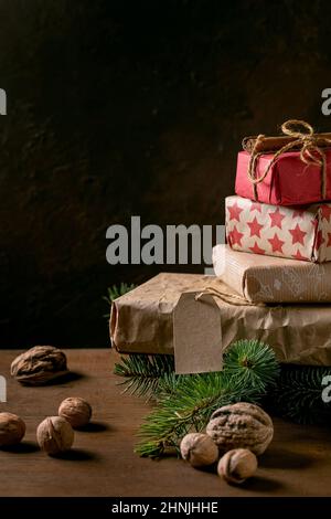 Collection de boîtes-cadeaux de Noël en papier artisanal écologique décoré de noix naturelles et de bâtons de cannelle sur une table en bois avec branches de sapin. E Banque D'Images