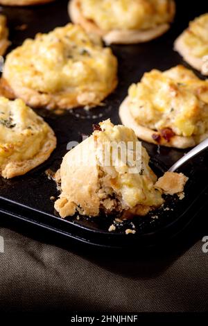 Gros plan de la traditionnelle viande hachée pâte sablée mini-tartes avec purée de pommes de terre et de thym sur la plaque de cuisson noire nappe en lin foncé, mur gris à Banque D'Images