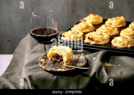 Entier et de commencer à manger maison viande hachée pâte courte mini tartes avec purée de pommes de terre et de thym dans un plateau de cuisson noir et un verre de vin rouge.Dar Banque D'Images