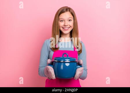 Portrait d'une jolie fille gaie portant un tablier de cuisine maison soupe isolée sur fond rose pastel couleur Banque D'Images