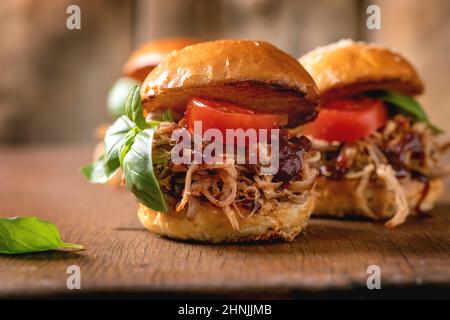 Gros plan de mini hamburgers faits maison avec ragoût de bœuf, tomates et basilic sur fond de bois.Restauration rapide moderne et délicieuse Banque D'Images