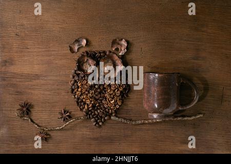 En forme de chouette, à partir de grains de café et d'épices. Owl s'assoit sur la branche avec une tasse de café sur fond de bois. Concept de café mystère amusant Banque D'Images