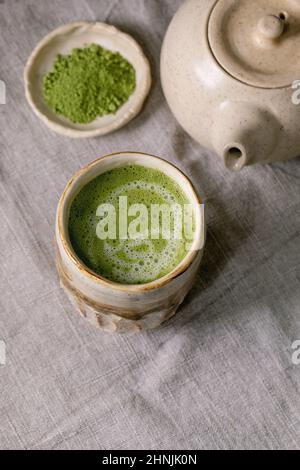 Latte traditionnelle japonaise au thé vert chaud et au matcha dans une tasse en céramique faite à la main, au matcha en poudre, à la théière et au fouet en bambou sur le tableau en lin gris Banque D'Images