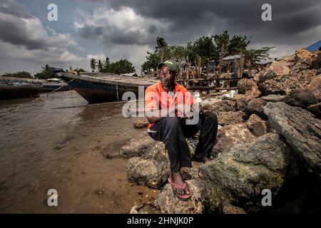 C'est Machamo c'est un pêcheur qui a vécu 35 ans dans un petit village de pêcheurs Kunduchi, près de Dar es salaam, en Tanzanie. Au cours des 7 dernières années, la mer montante a mangé loin à la plage avançant 35 mètres et est maintenant à quelques mètres de sa maison et du village. Dans une tentative désespérée de protéger son village, il a construit une défense contre les vagues en utilisant du bois de grève et des sacs pleins de déchets en plastique qui se lave sur les rives. Il sait que cela ne va pas vaincre la montée des vois, mais lui et sa famille n'ont pas d'autre endroit où aller. Banque D'Images