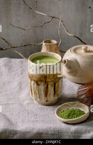 Latte traditionnelle japonaise au thé vert chaud et au matcha dans une tasse en céramique faite à la main, au matcha en poudre, à la théière et au fouet en bambou sur le tableau en lin gris Banque D'Images