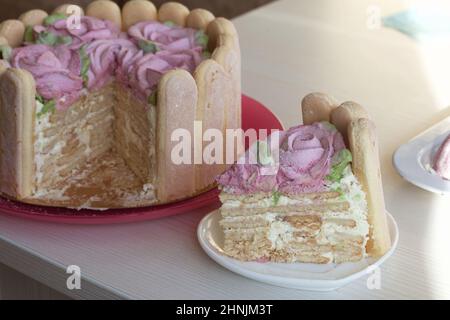 Gâteau avec biscuits Savoiardi et roses guimauves. Un morceau de gâteau est coupé. Attaché avec ruban. Le ruban est attaché dans un noeud. Banque D'Images