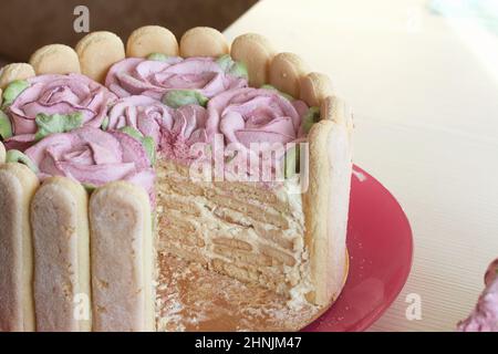 Gâteau avec biscuits Savoiardi et roses guimauves. Un morceau de gâteau est coupé. Attaché avec ruban. Le ruban est attaché dans un noeud. Banque D'Images