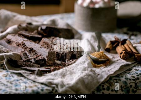 Ingrédients pour faire chocolat chaud boisson d'hiver. Chocolat noir haché, espèces, sucre de canne, sur la nappe de linge rustique dans la cuisine campagnarde. Banque D'Images