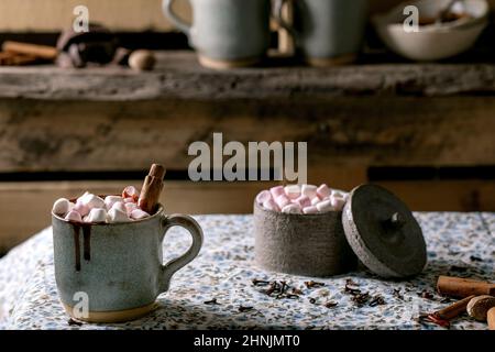 Une tasse de boisson d'hiver au chocolat chaud et épicé avec guimauve, bâton de cannelle, épices et un pot de guimauve sur une nappe en lin rustique.Pays k Banque D'Images