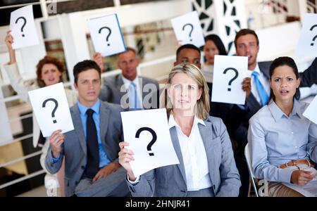 Arrêtez de nous laisser dans l'obscurité. Photo d'un groupe d'hommes d'affaires tenant des panneaux avec des points d'interrogation sur eux pendant une présentation de travail. Banque D'Images