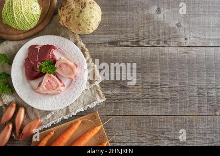 Ingrédients pour préparer du bouillon de bœuf ou de la soupe - os de moelle et légumes frais sur fond de bois avec espace de copie Banque D'Images