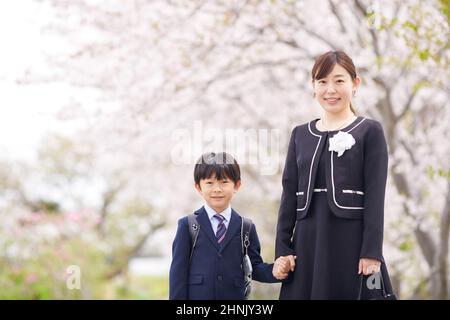 École primaire japonaise Boy et sa mère sous les cerisiers en fleurs Banque D'Images