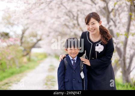 École primaire japonaise Boy et sa mère sous les cerisiers en fleurs Banque D'Images