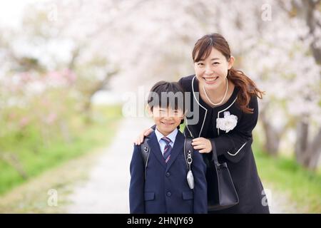 École primaire japonaise Boy et sa mère sous les cerisiers en fleurs Banque D'Images