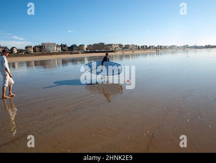 Un touriste sur la plage avec sa planche de surf à Saint-Malo, Bretagne, France Banque D'Images