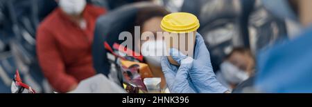 Gros plan des mains dans les gants de protection du préposé aux vols servant des boissons aux passagers à bord. Voyager en avion pendant la pandémie de Covid19 Banque D'Images