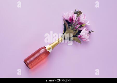 Bouteille de champagne de rose avec des fleurs disposées en diagonale sur un fond violet avec espace de copie Banque D'Images
