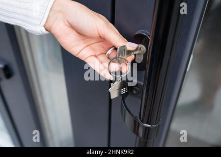 La main d'une femme ouvre la porte avec une clé sur laquelle le porte-clés est accroché à la maison et copie l'espace. Banque D'Images