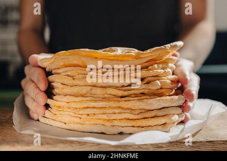 Les petits gâteaux ronds de lavash sont empilés, les mains de cuisinier étirent lavash vers l'avant pour les tests. Gros plan sur le pain plat espagnol ou le lavash arménien Banque D'Images