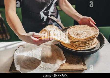 les mains de baker sont en retrait de pain pita d'une poêle en fonte. Petite boulangerie privée produisant du pain artisanal et du pain pita. baker en tablier dans la cuisine Banque D'Images